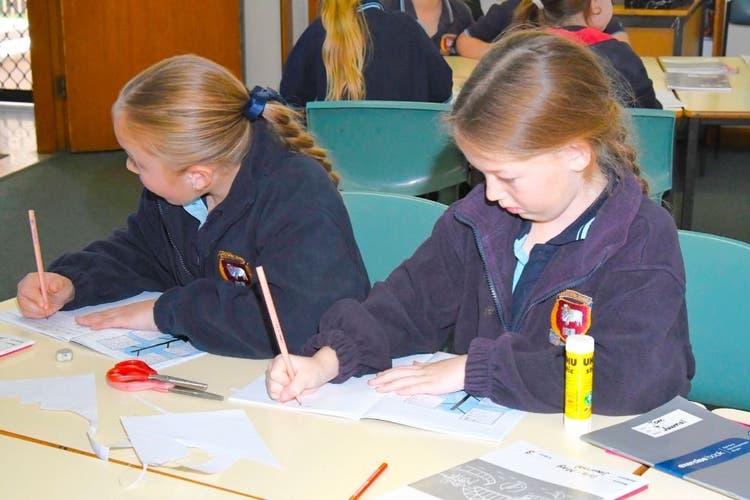 Two students writing in exercise books at a desk